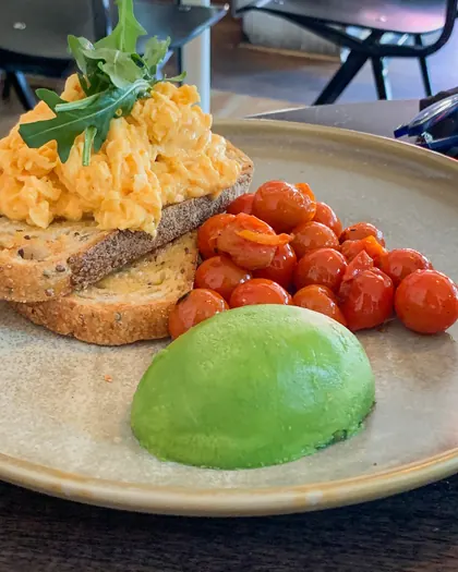 Scrambled eggs on multigrain toast with avocado, roast tomatoes and rocket