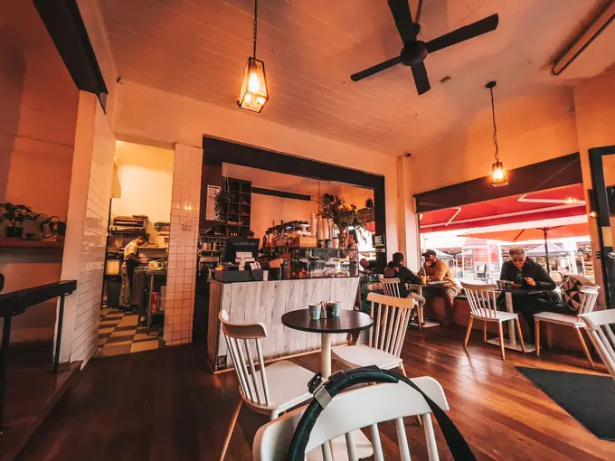 The dining room with pendant lanterns, white bistro chairs and timber floors, looking out to the red awning
